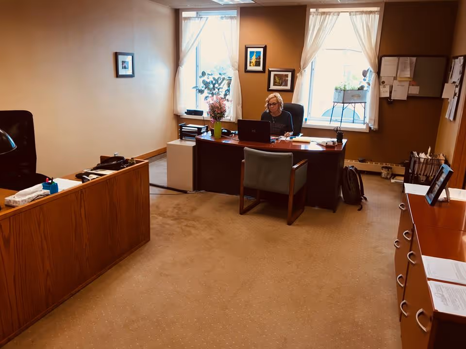Office in a senior living facility with a person seated at a desk, computer, and plants.