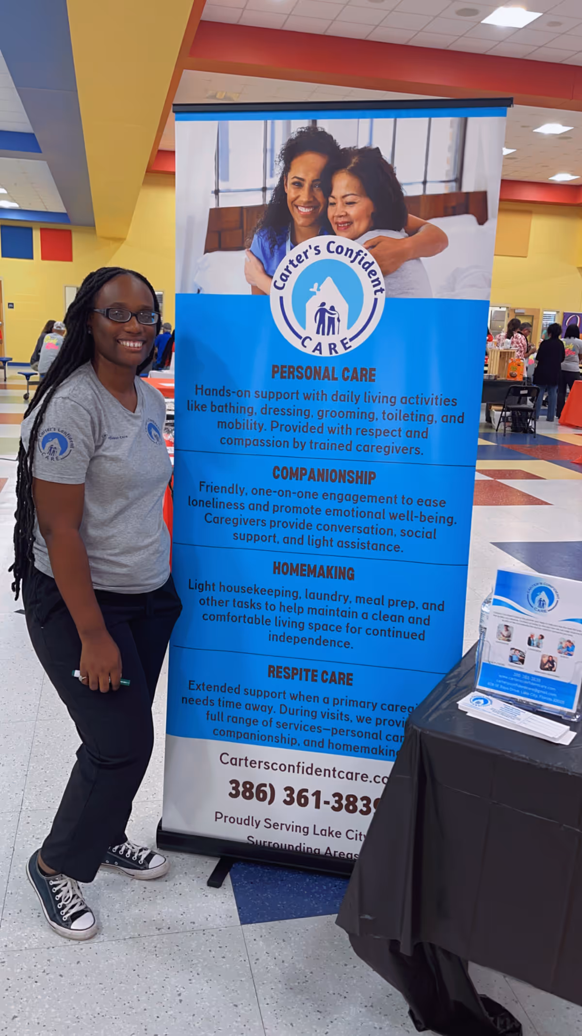 Caregiver in gray shirt stands beside a Carter's Confident Care banner in a colorful indoor space.