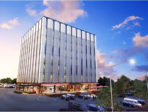 Modern glass-fronted building with a curved entrance and surrounding parking.