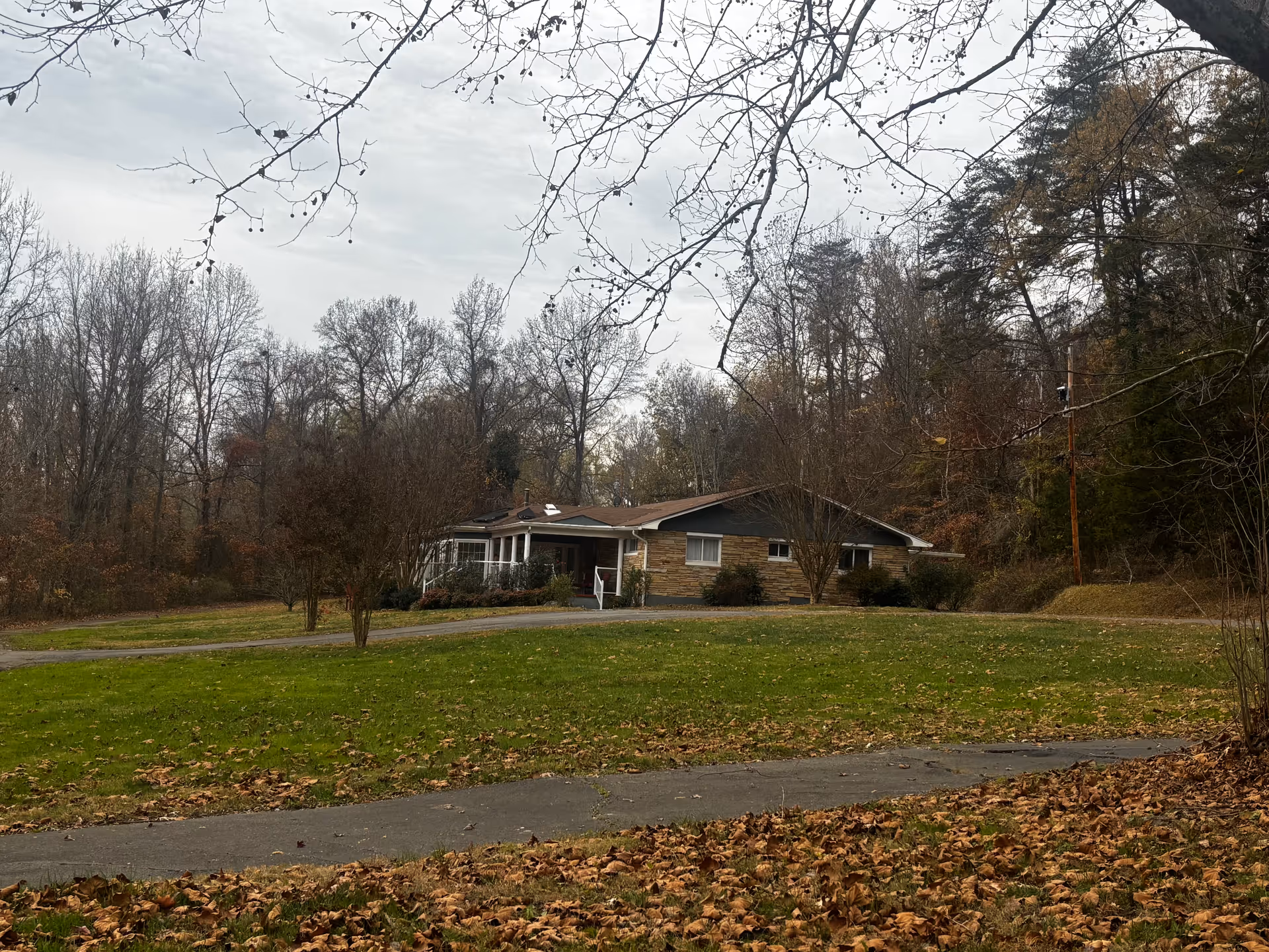 Single-story brick ranch-style house with a front lawn and trees under an overcast sky.