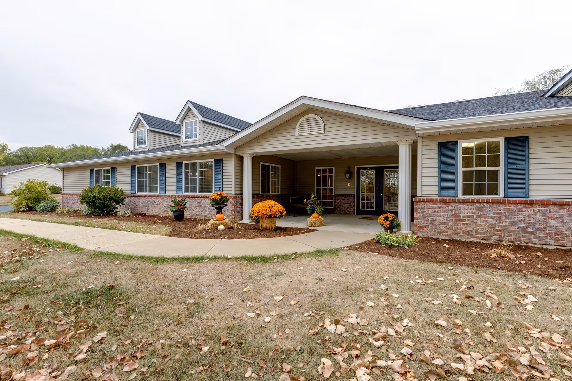Single-story senior living facility exterior with a covered entrance and autumn decorations.