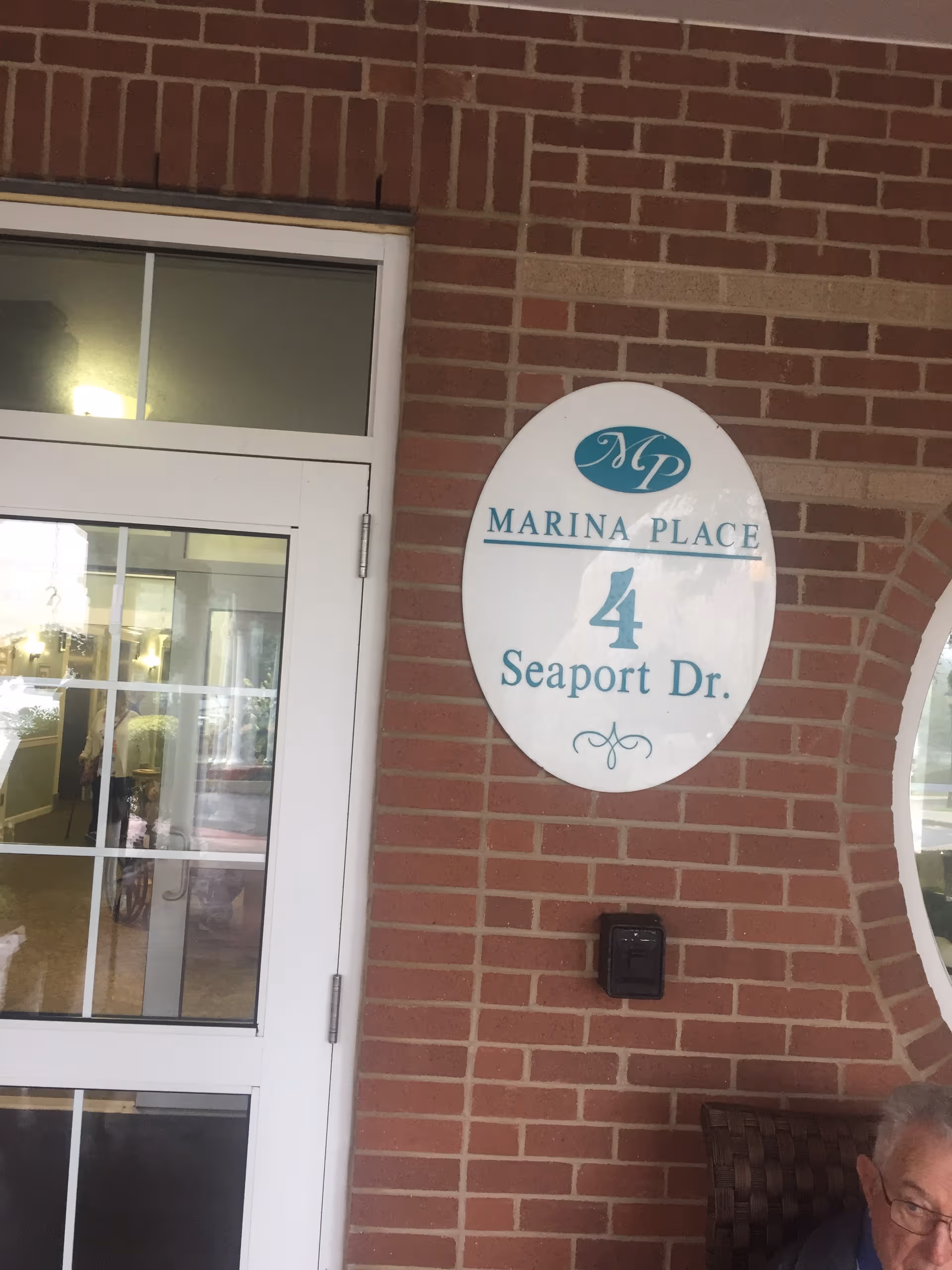 Brick exterior entrance of Marina Place with an oval sign and glass doors.