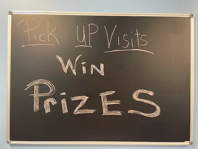Chalkboard in a light-blue interior displays 'Pick Up Visits Win Prizes'.