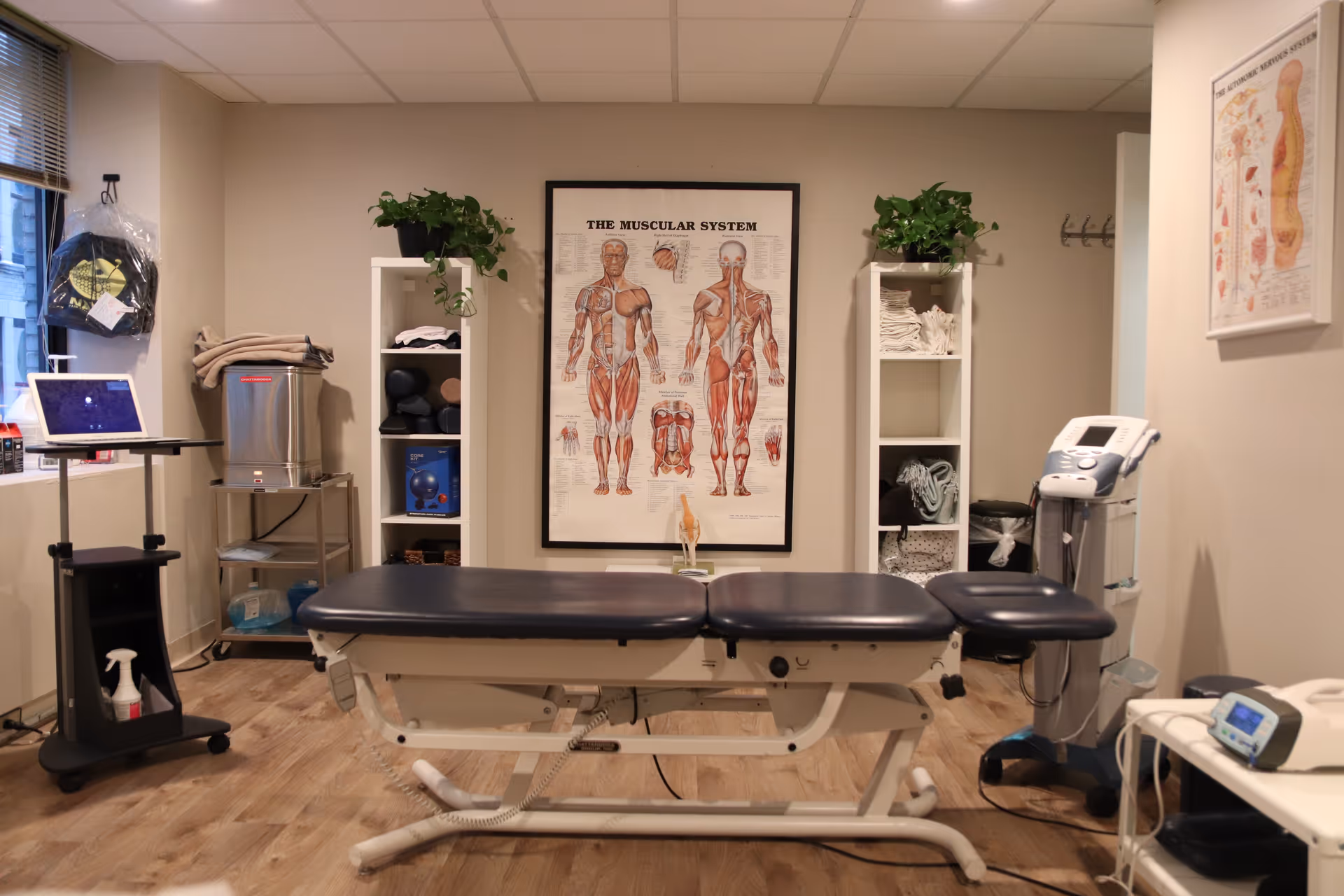Physical therapy treatment room with examination table, medical equipment, and anatomical poster.