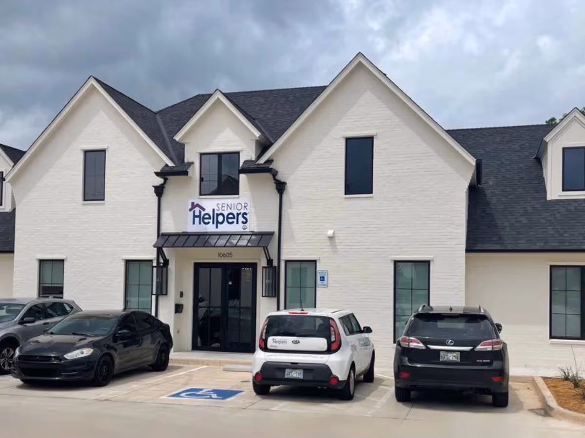 Exterior front view of Senior Helpers facility with white brick, sign, and parked cars.