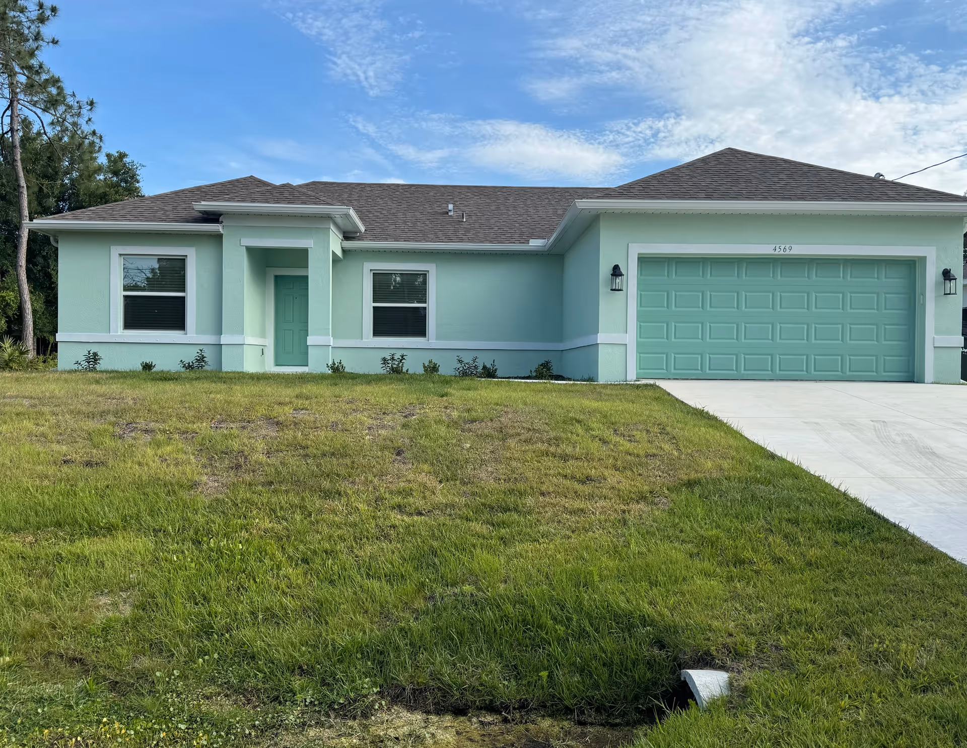 Mint-green single-story house with a two-car garage and front lawn under blue sky.