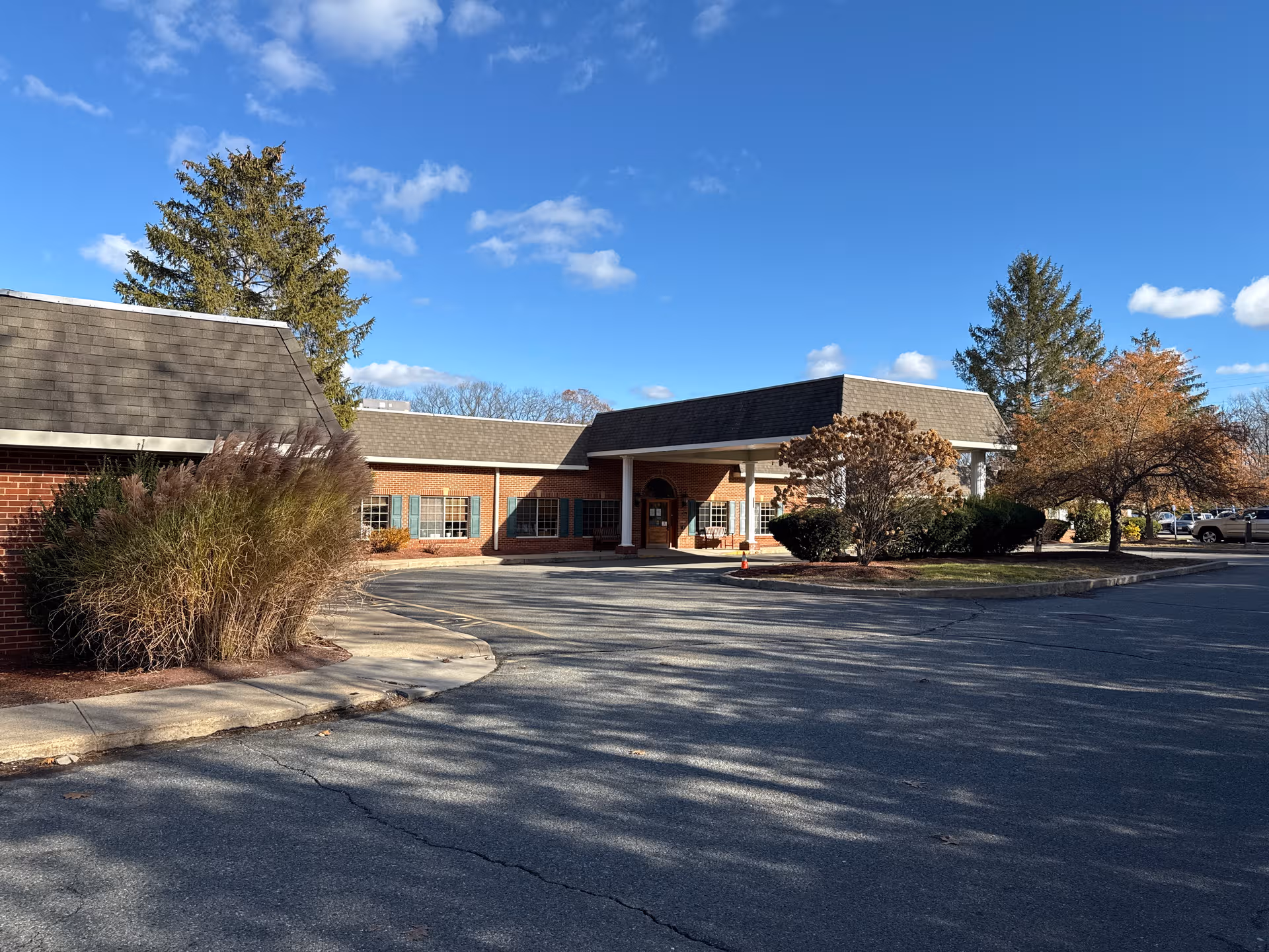 Exterior view of a brick senior living facility with a covered entrance and a parking lot.