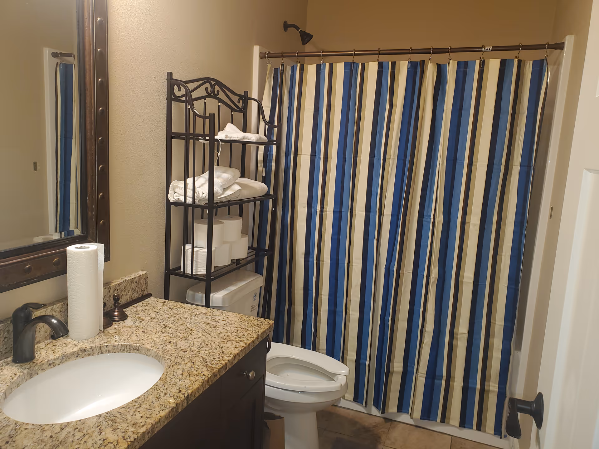 Bathroom with sink, mirror, toilet, metal towel shelf, and blue striped shower curtain.