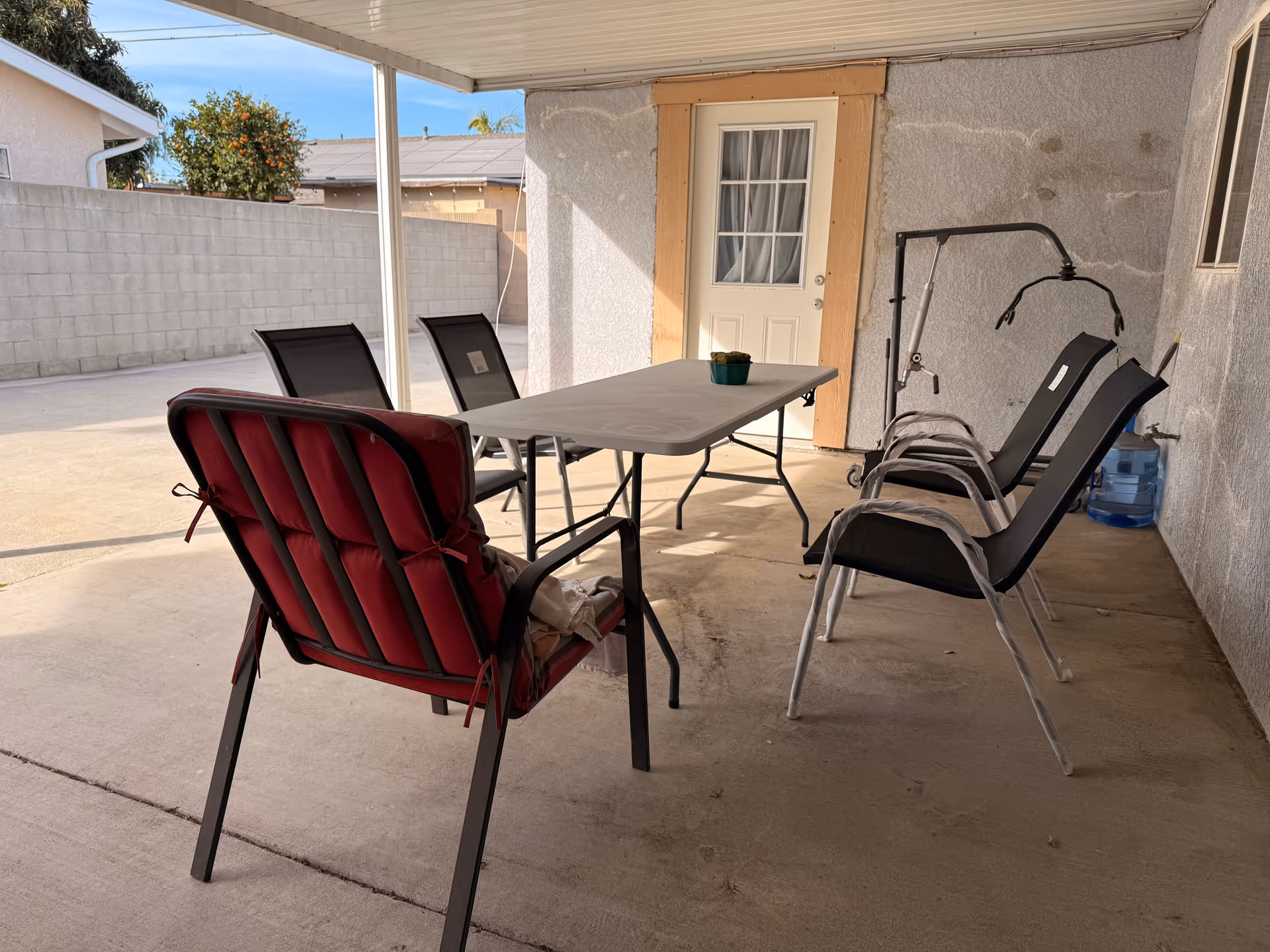 Outdoor covered patio with table, chairs, and water cooler against the wall.