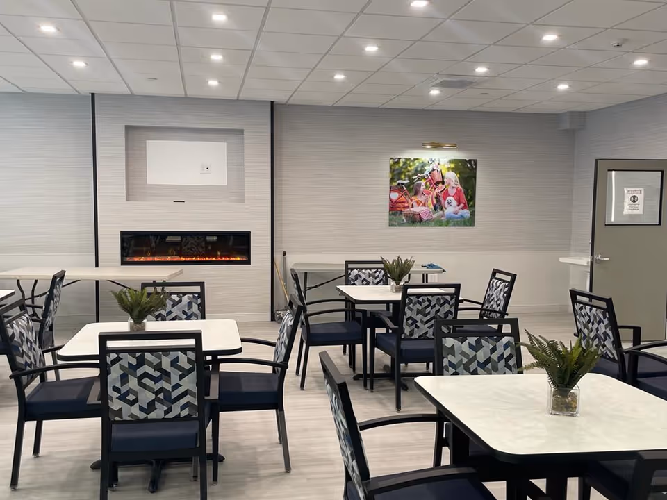 Teaneck Nursing Center dining room with white tables, patterned chairs, and potted plants.