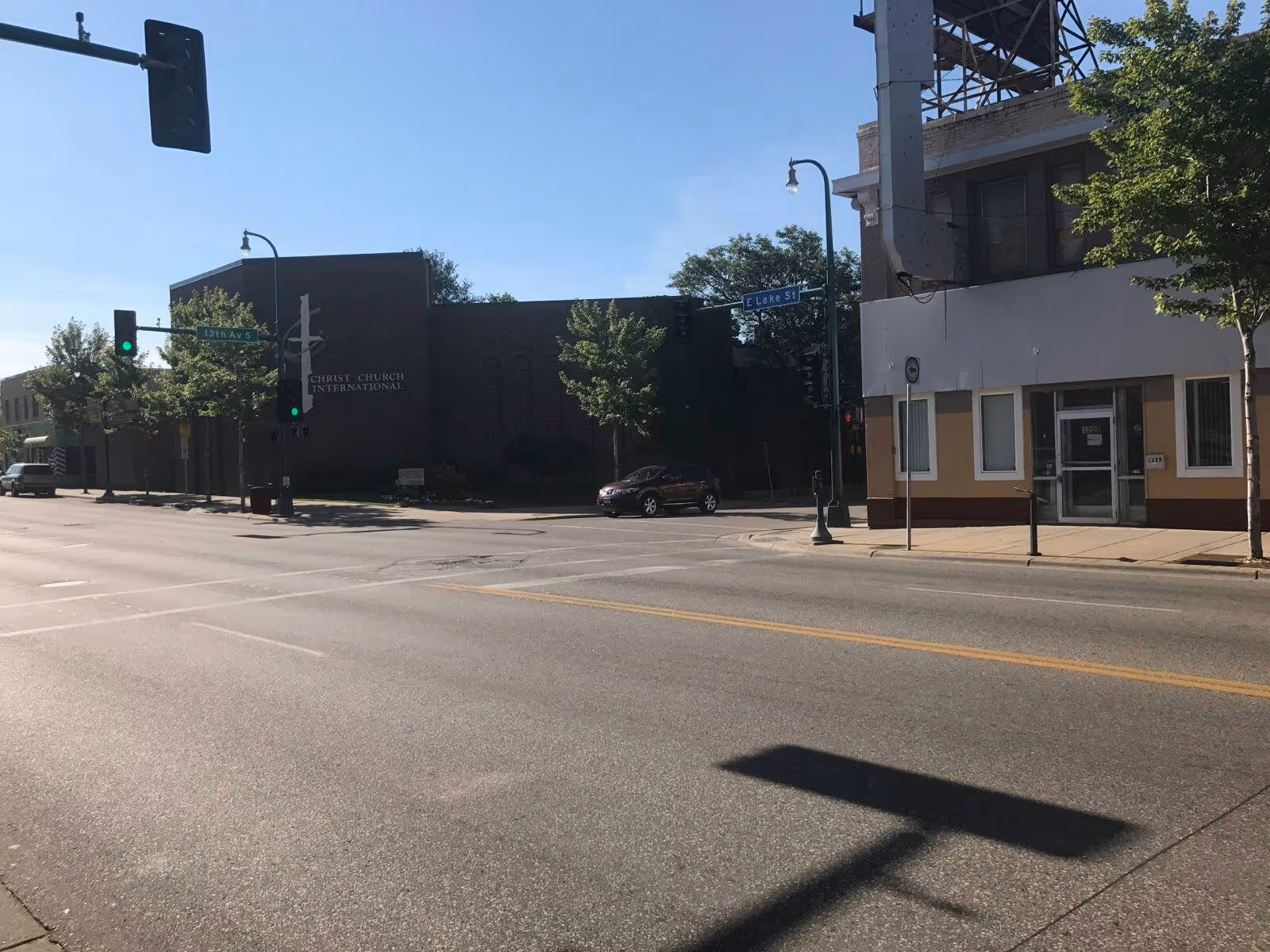 Street corner with storefronts, traffic lights, and a parked car on sunny day.