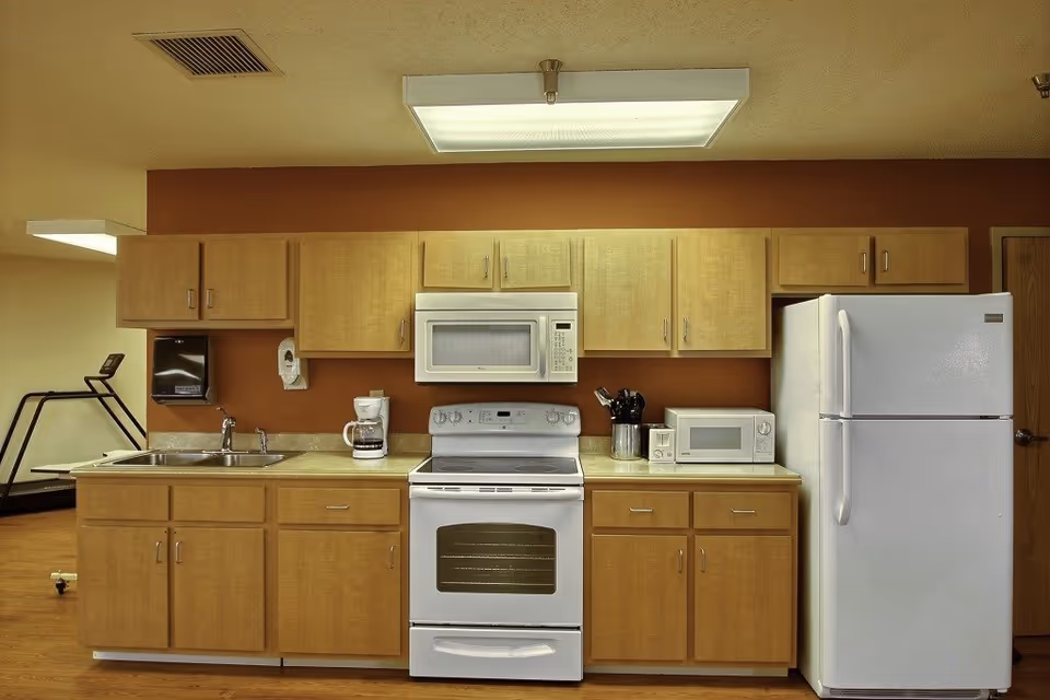 Senior living facility kitchen with wooden cabinets and white appliances.