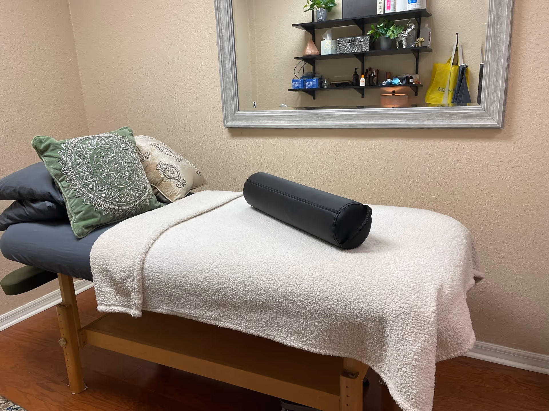 A massage therapy table in an interior room with a mirror and shelves.