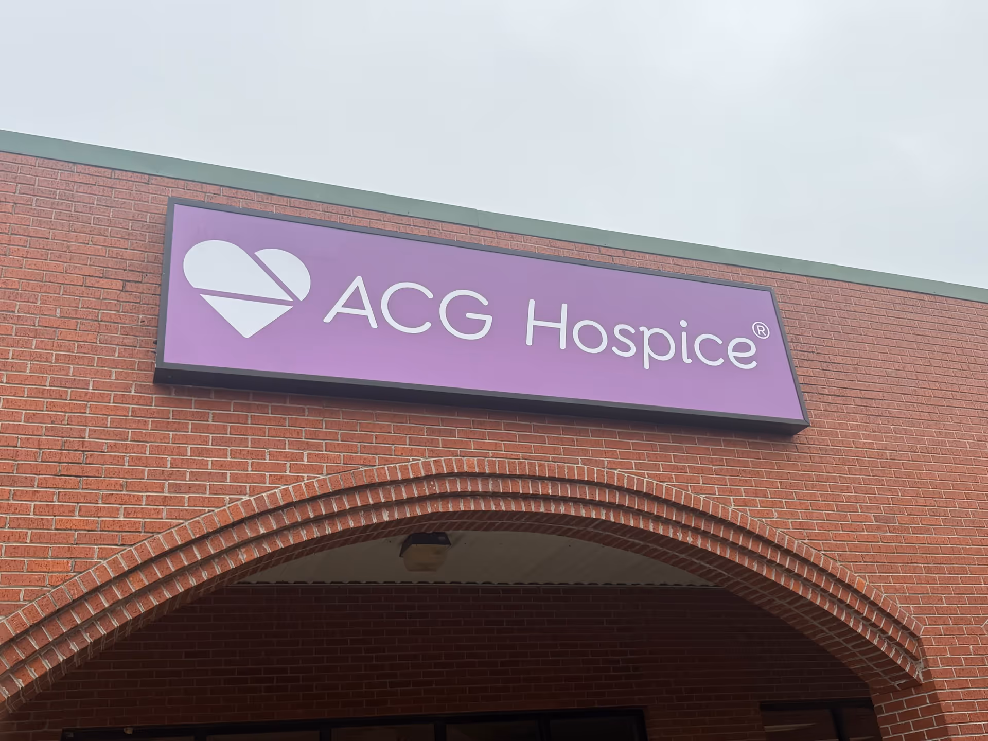 Brick building exterior with a purple ACG Hospice sign above an arched entrance.