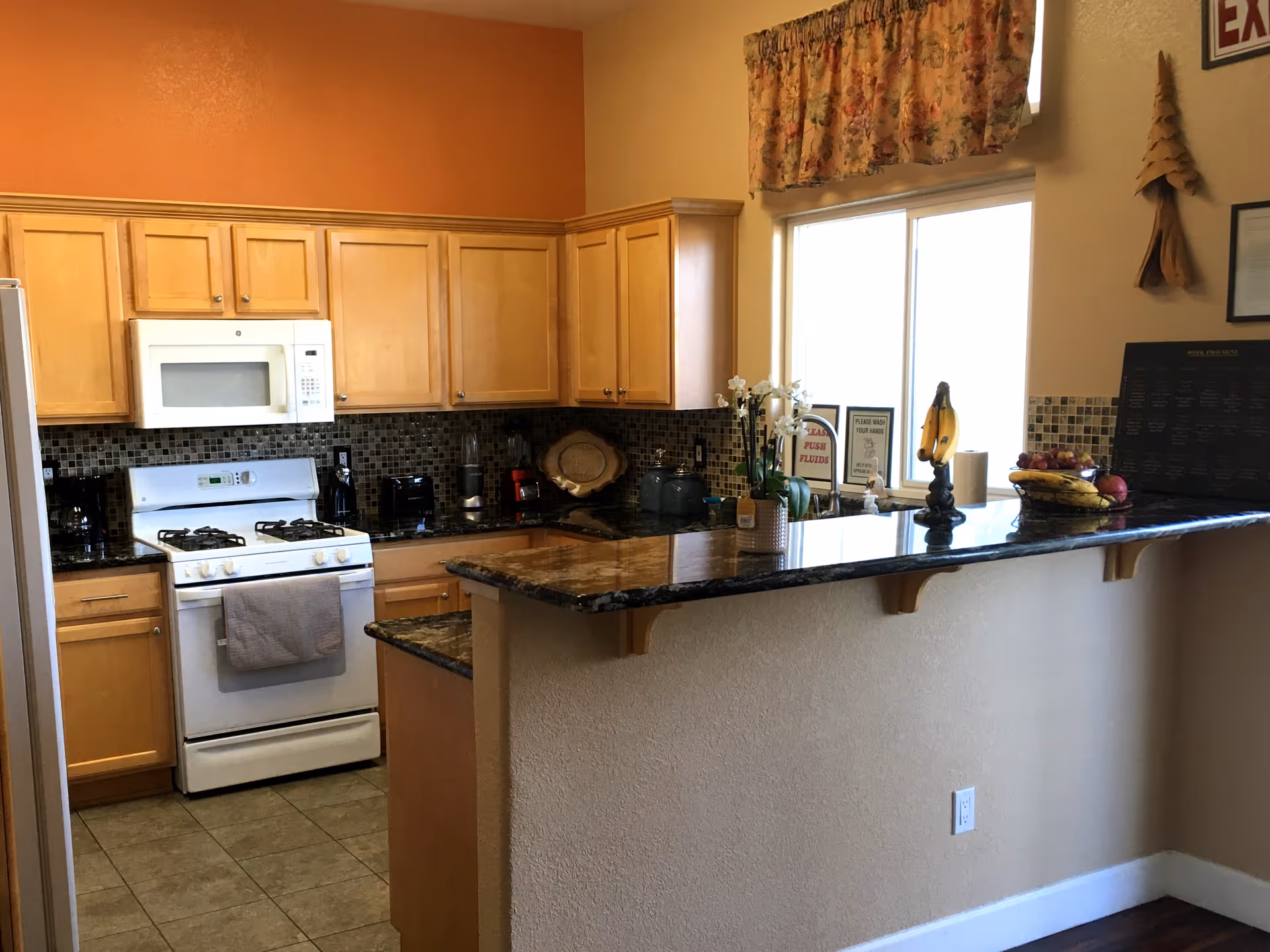Bright kitchen with wooden cabinets, white appliances, and a granite-topped bar counter.