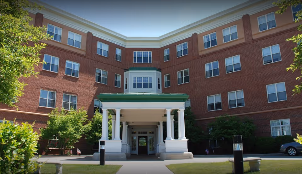Brick senior living building with white columns and a green roofed entrance