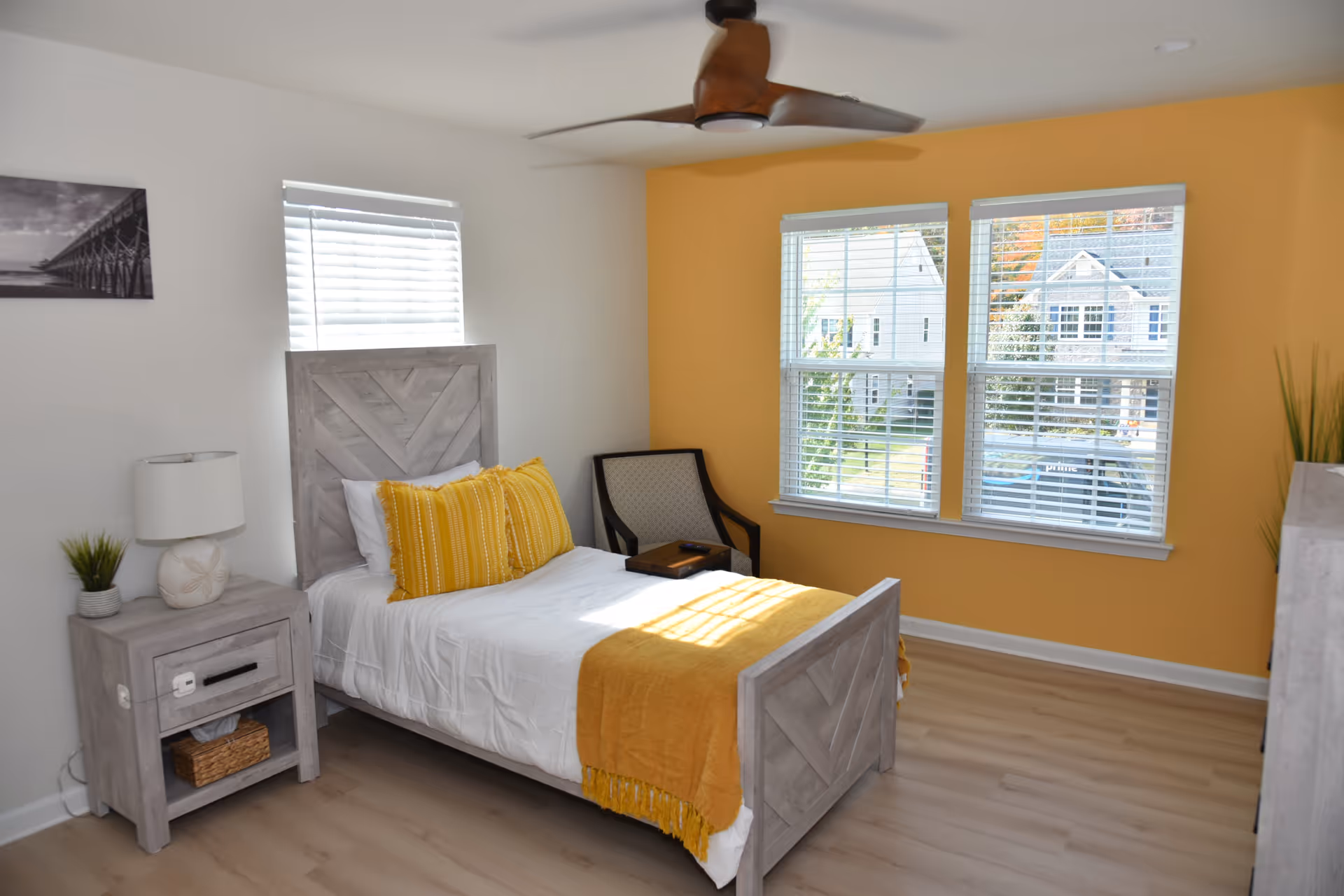 A bright bedroom with a gray wood bed, yellow accents, and two large windows.