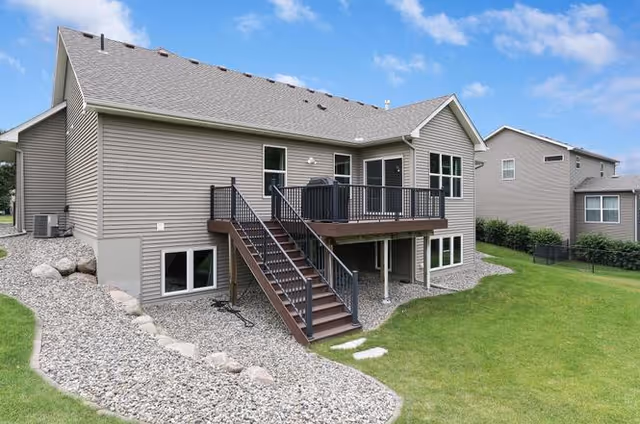Exterior view of a beige two-story senior living building with a wooden deck and lawn.
