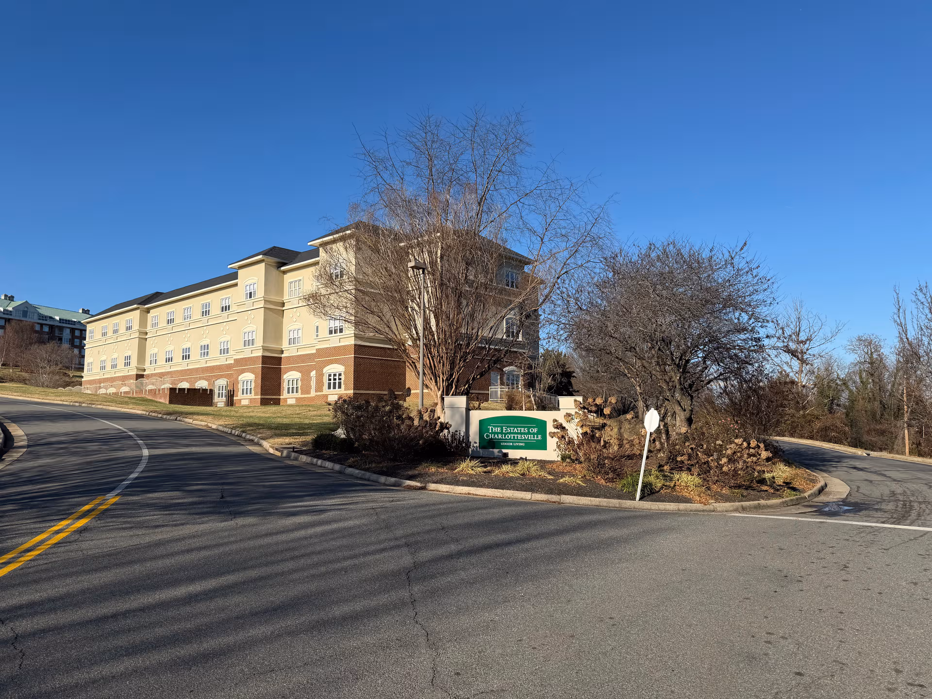 Exterior view of a multi-story senior living building with a curved driveway and sign.