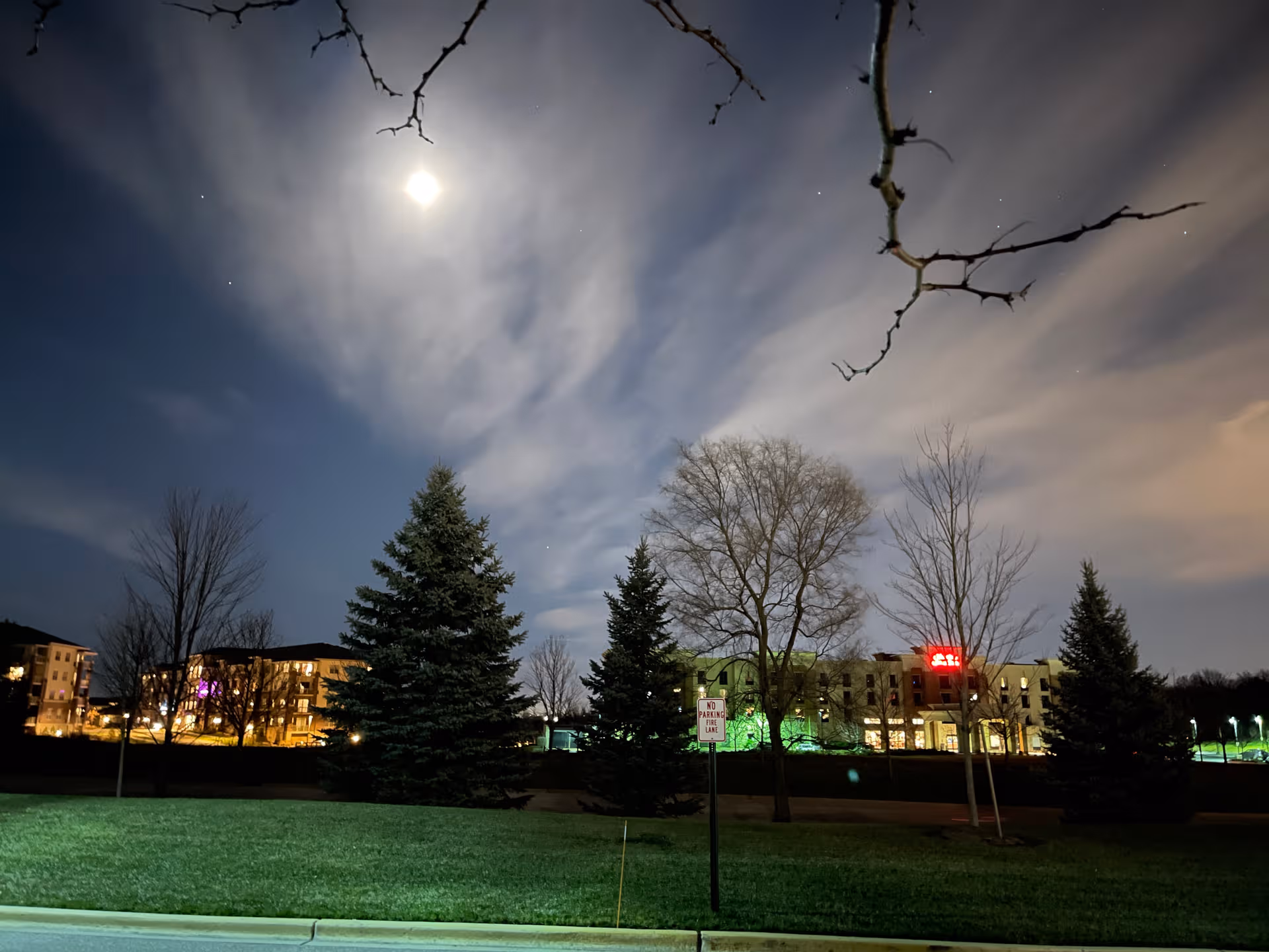 Night exterior of a senior living campus with trees, buildings, and a grassy foreground.
