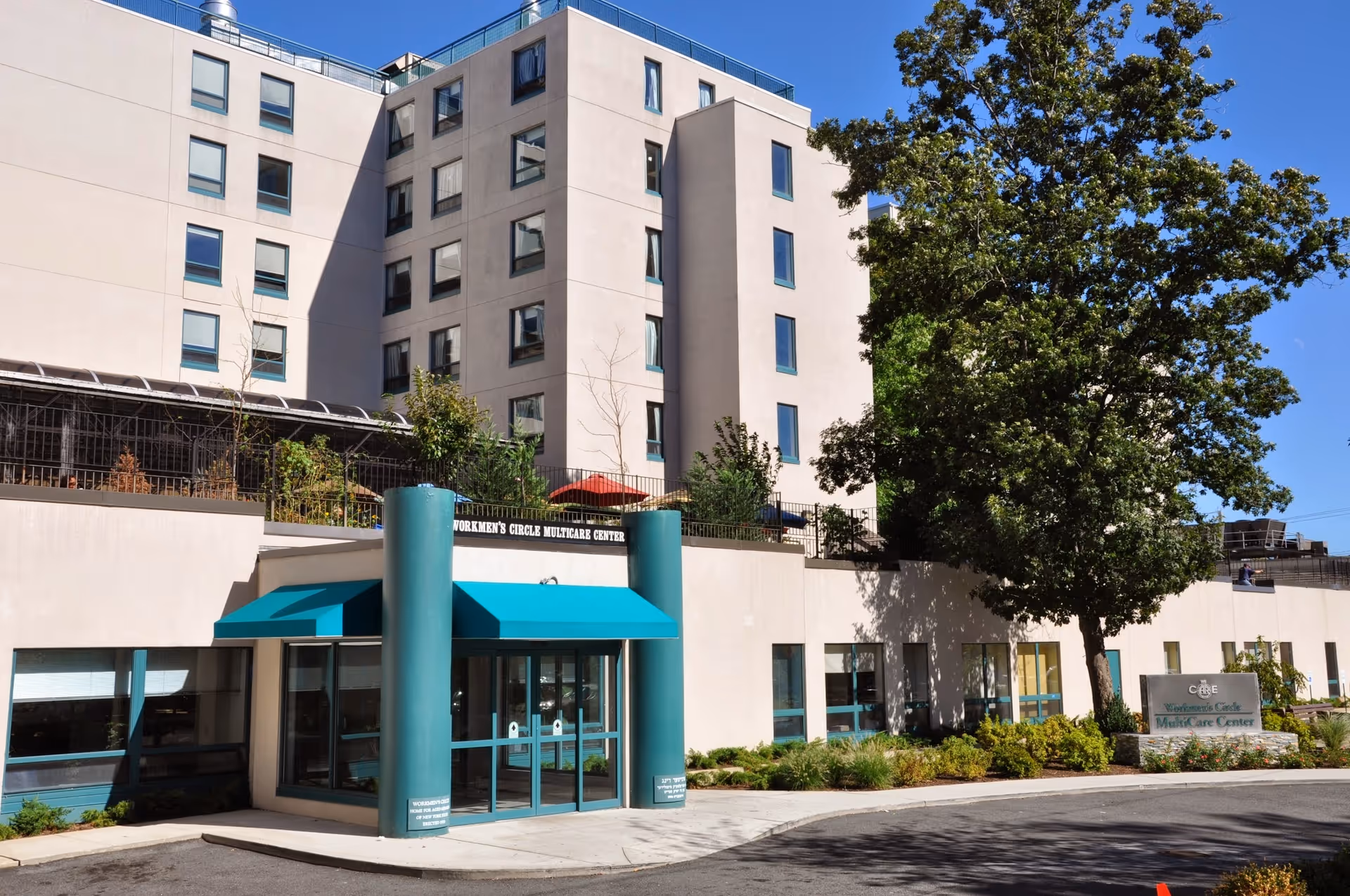 Front exterior of a modern senior living center with teal entrance canopy.