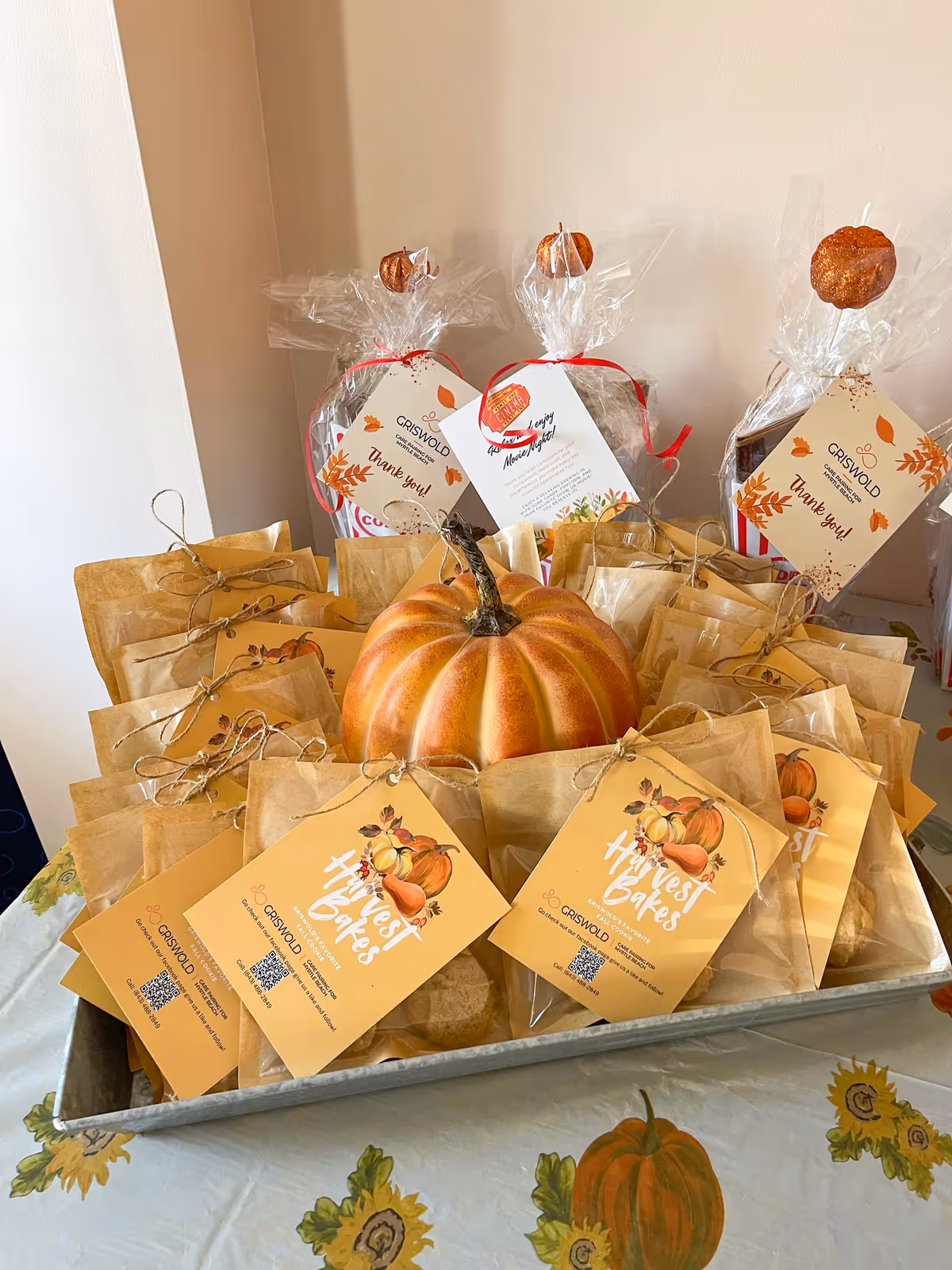 A large pumpkin centerpiece surrounded by autumn gift bags and notes on a table.