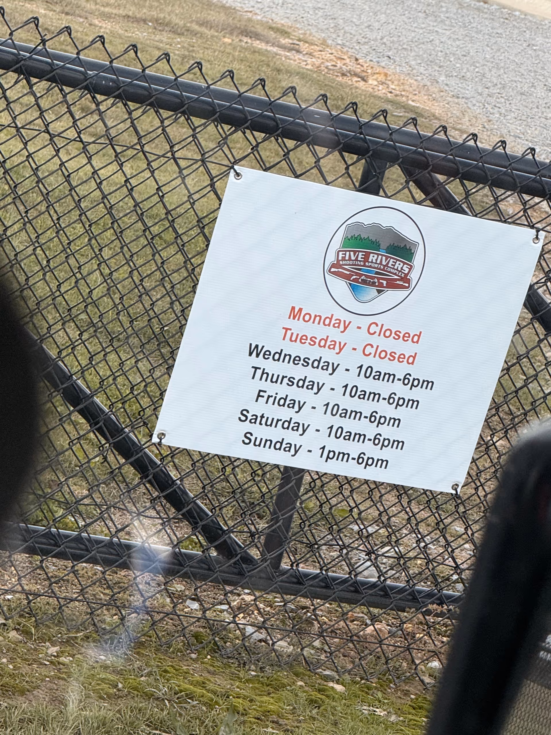 A sign on a chain-link fence shows Five Rivers hours for Monday through Sunday.