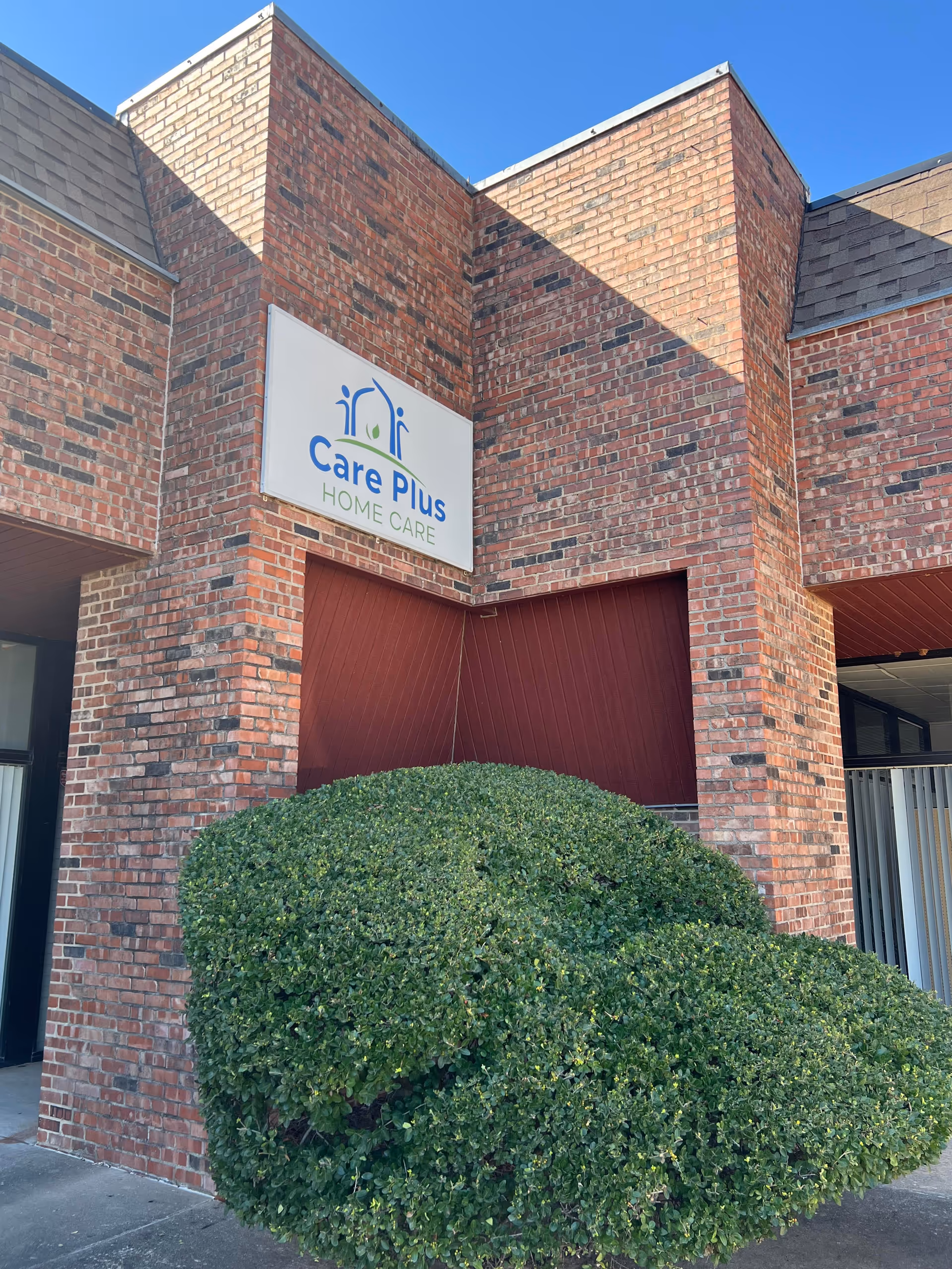 Front view of a brick building with a Care Plus Home Care sign and trimmed shrub.
