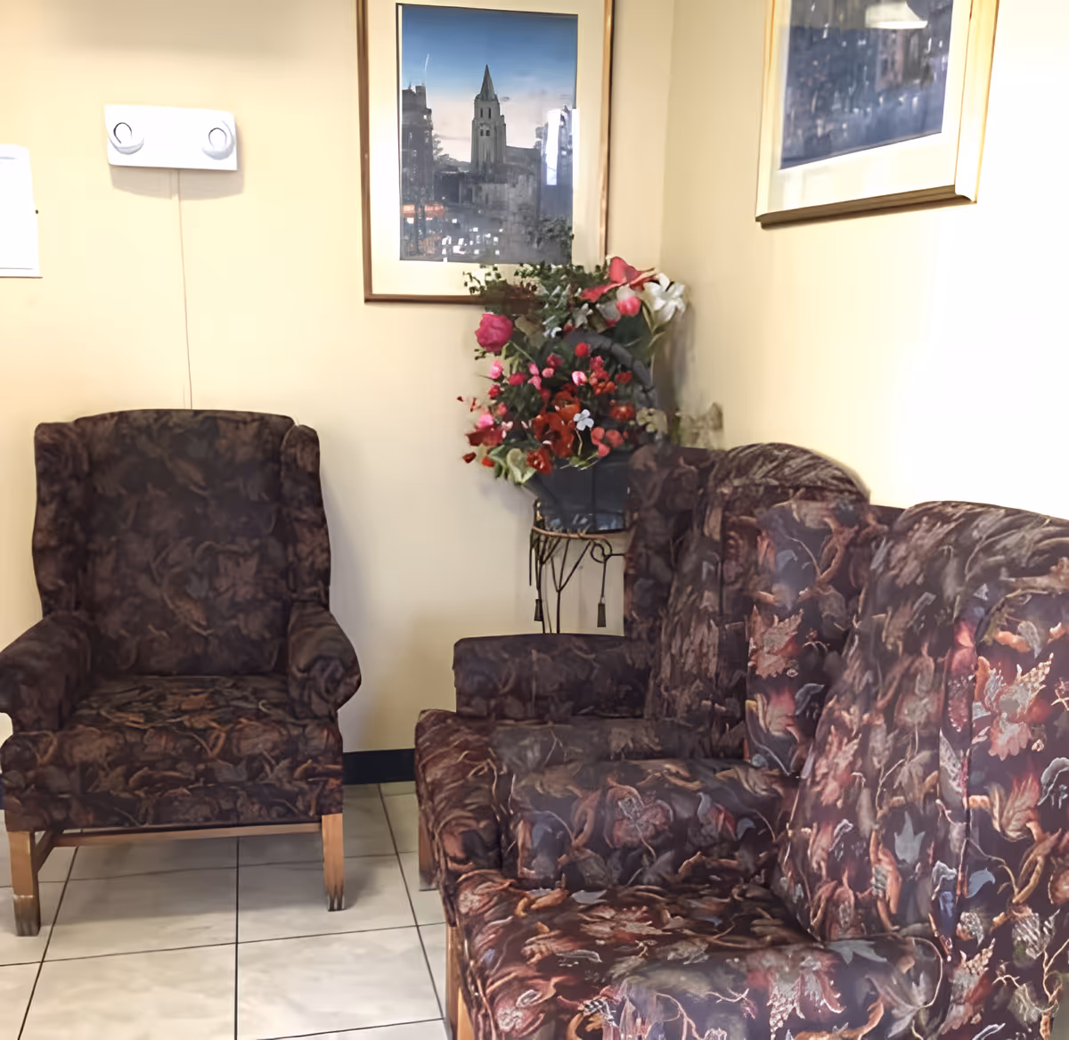 Upholstered patterned armchairs and a loveseat in a small waiting area with framed artwork and a floral arrangement.
