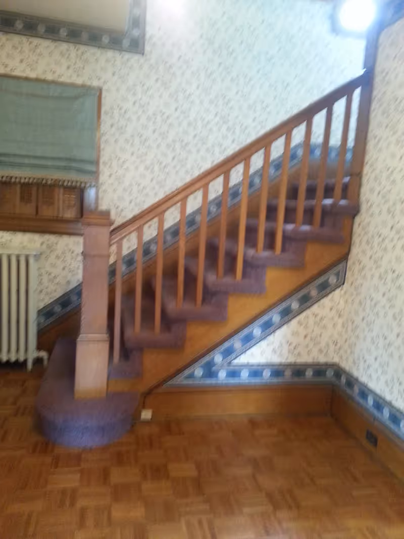 Wooden staircase with purple carpeted steps and a banister against floral wallpaper above a parquet floor.