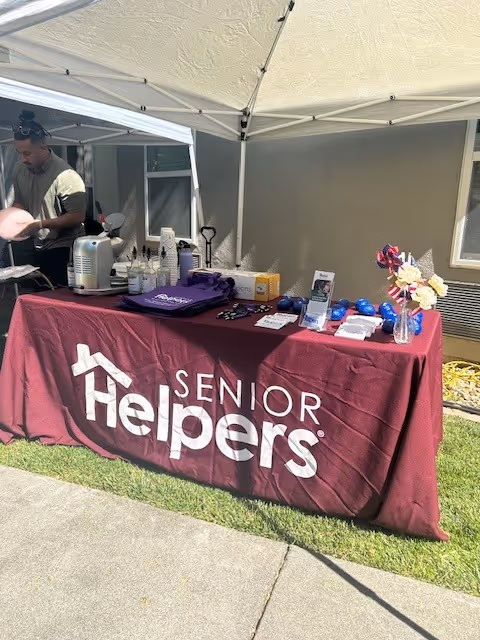 Outdoor booth setup by Senior Helpers with a table covered in maroon cloth under a canopy.