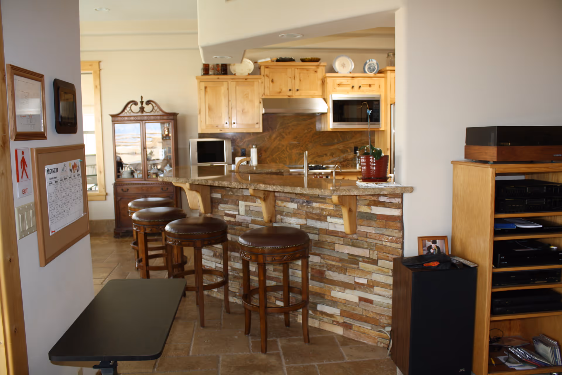 Interior kitchen with stone-front bar, wooden stools, and built-in appliances in a living center.