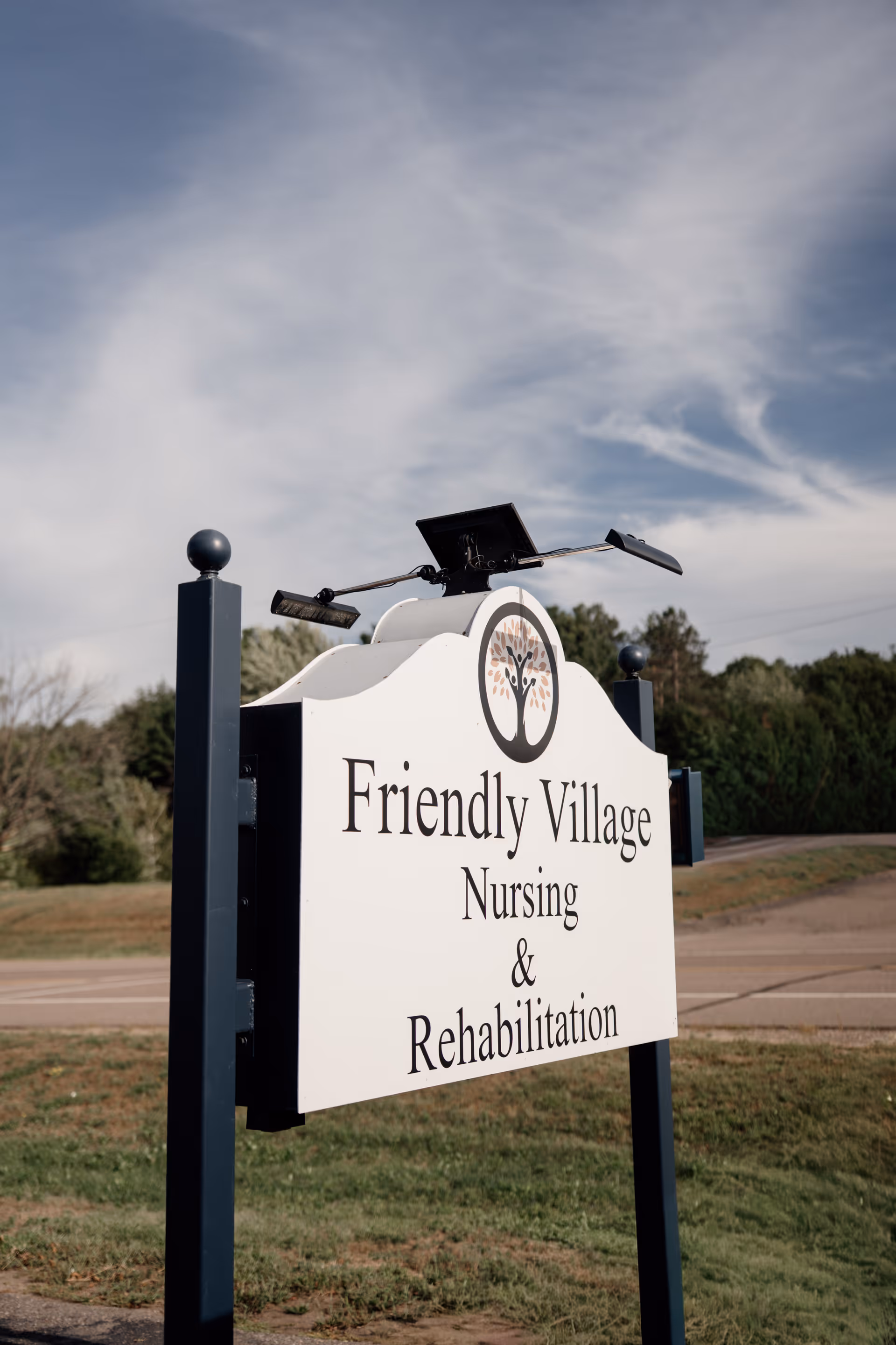 White signboard reading Friendly Village Nursing & Rehabilitation on a grassy front lawn.