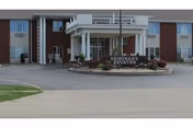 Exterior view of a senior living facility entrance with a sign and landscaped entry.