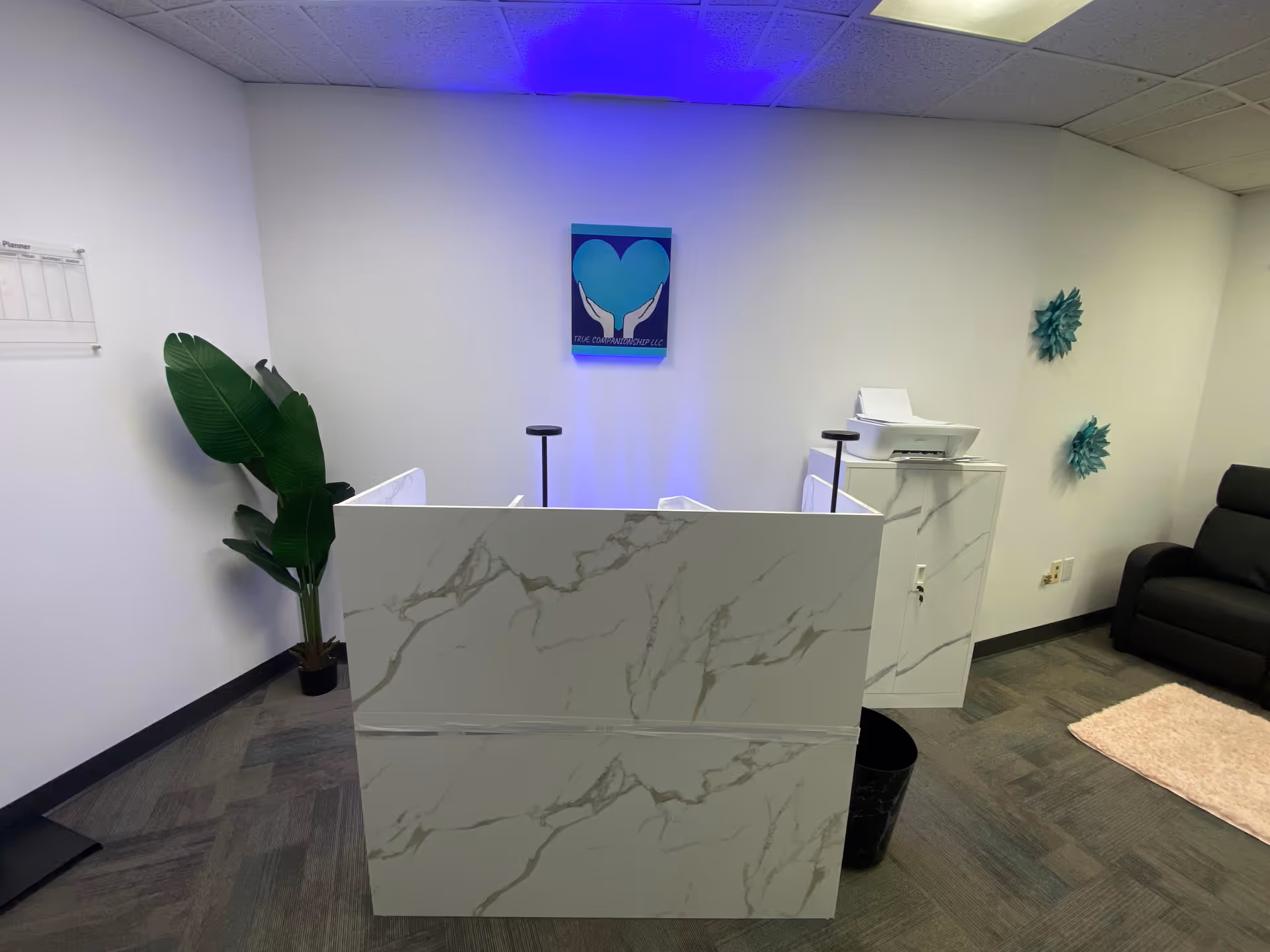 Reception area with marble front desk, printer, plant, and seating in a modern lobby.