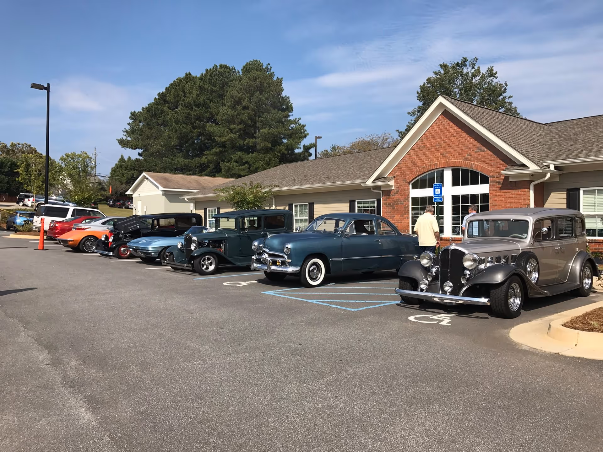 Front of Gaines Park Senior Living building with a row of vintage cars parked in the lot and two people near the entrance.