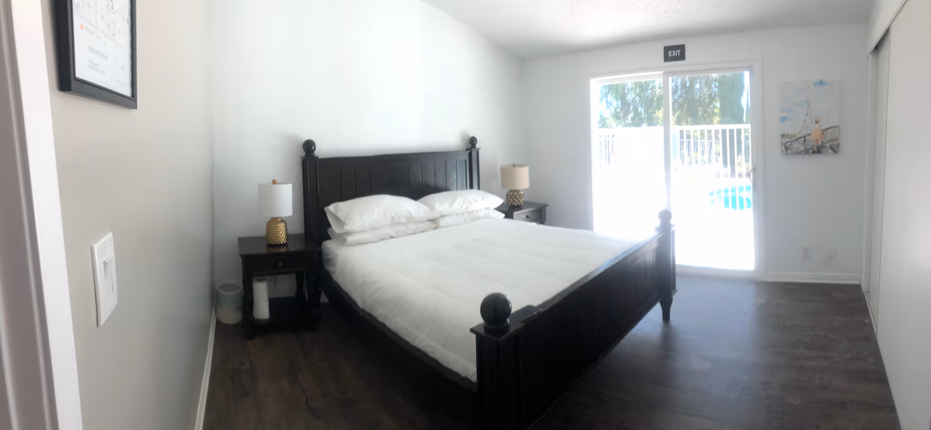 Dark wooden bed with white linens in a bright bedroom with a sliding door.
