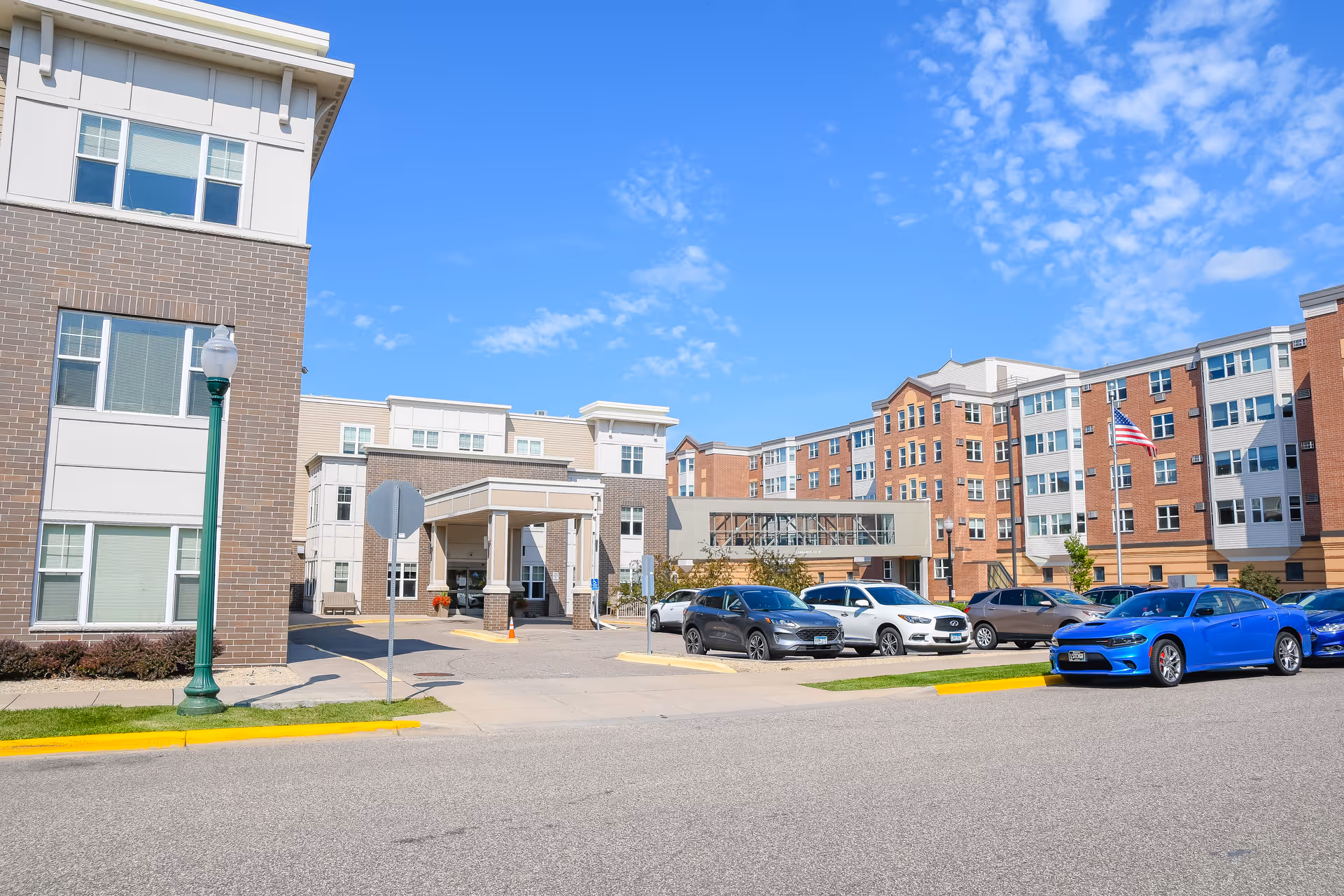 Exterior view of Plaza Gardens senior living facility with parked cars and entrance canopy.