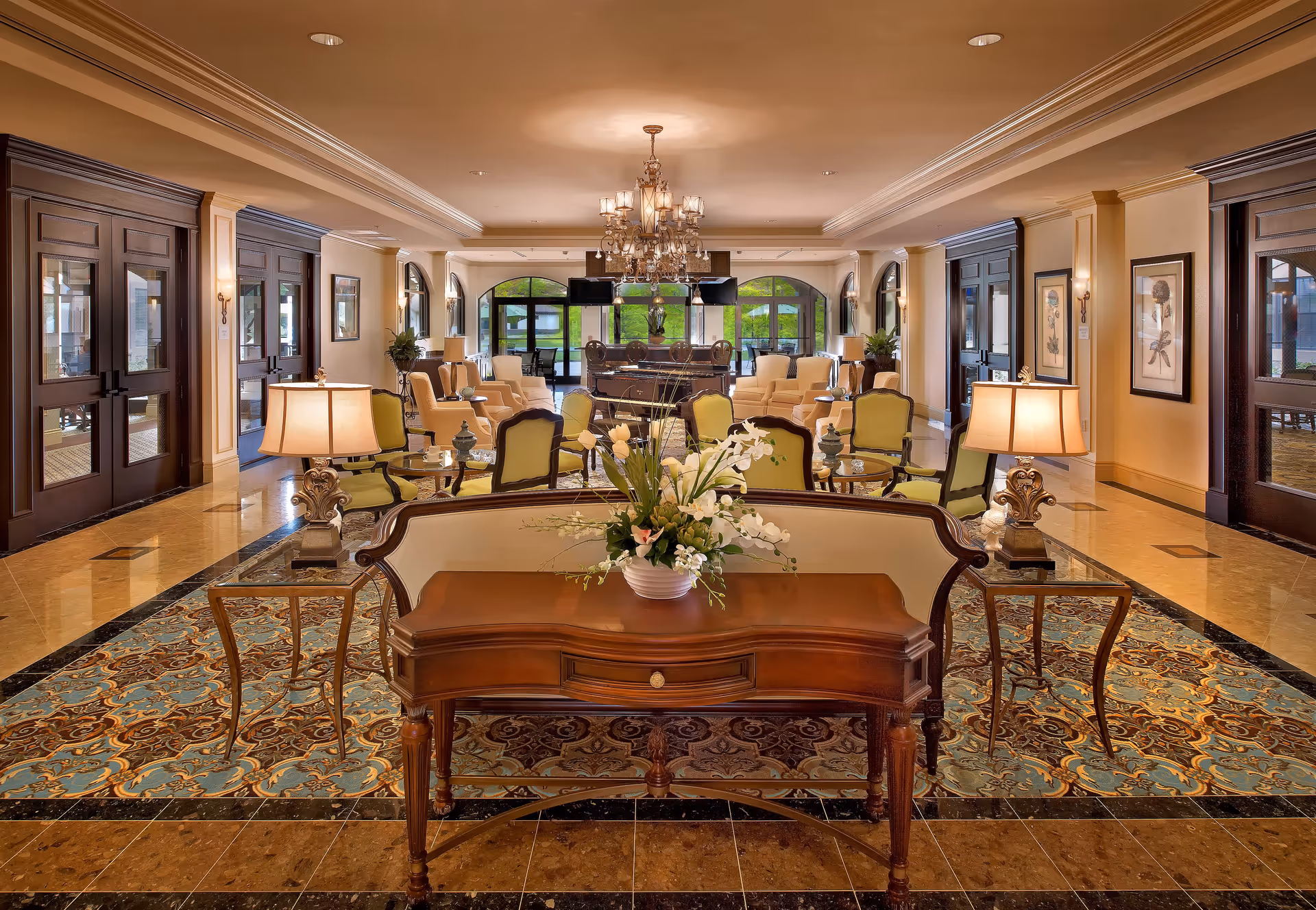 Spacious elegant lobby/lounge with sofas, armchairs, side tables, lamps, chandeliers, and a central floral arrangement.