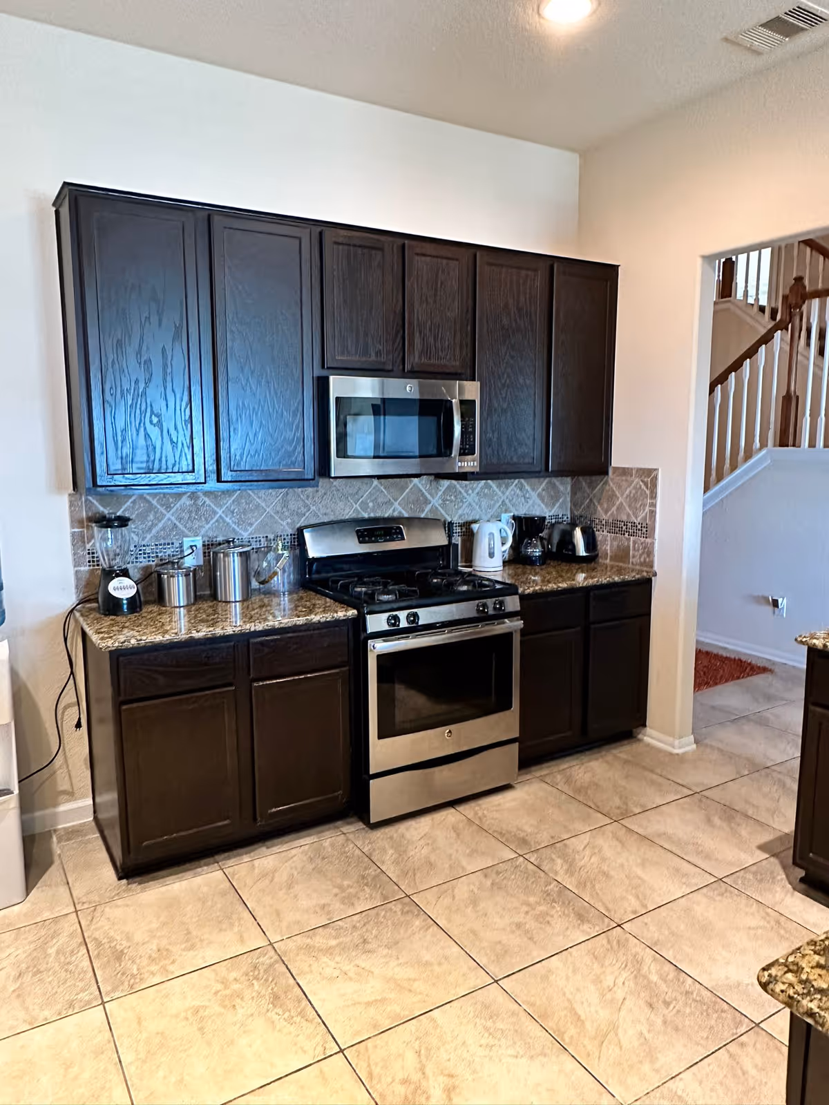Modern kitchen at Aurora Living Seniors with dark cabinets, granite counters, stainless appliances, and a staircase.