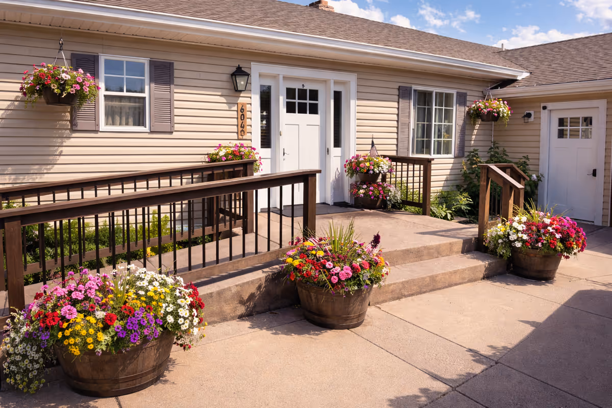 Front entrance of a beige, single-story facility with flower-filled planters and wooden railings.