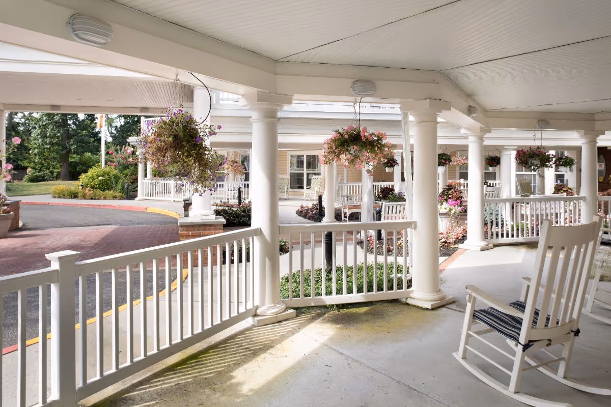 Covered front porch with white columns, rocking chairs and hanging flower baskets overlooking the facility driveway.