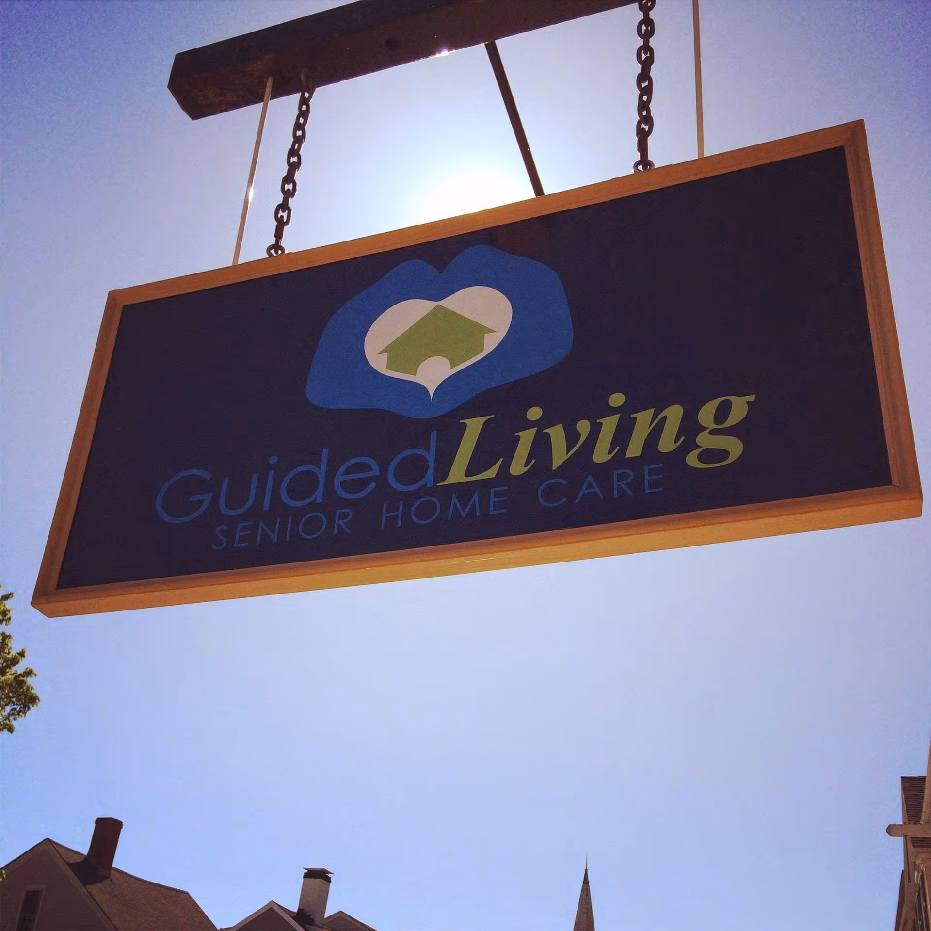 A hanging sign reads Guided Living Senior Home Care against a clear blue sky.