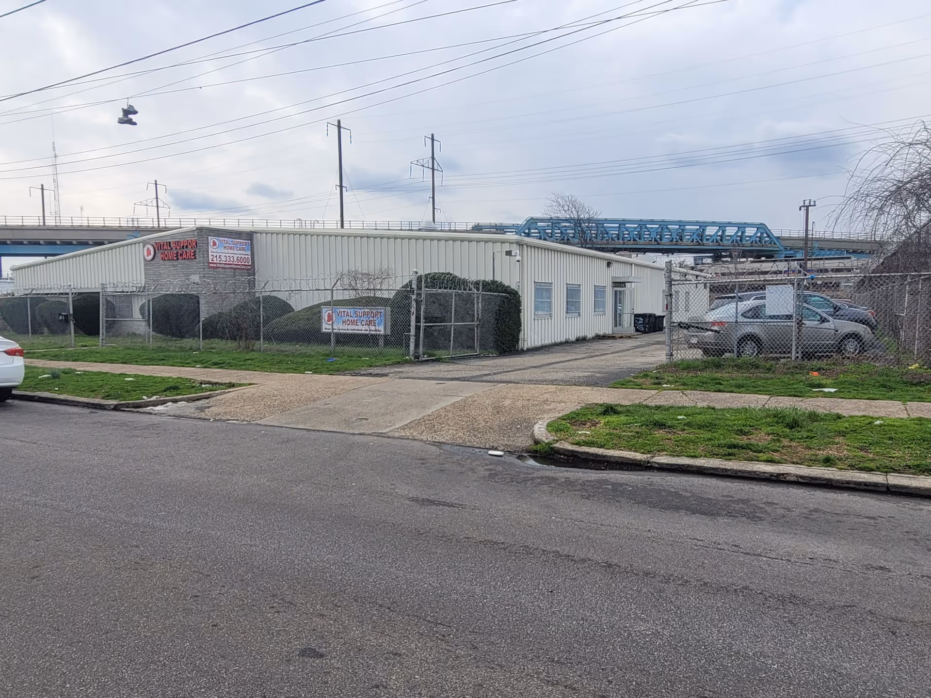 Front exterior of Vital Support Home Care Agency with chain-link fence and parked cars.
