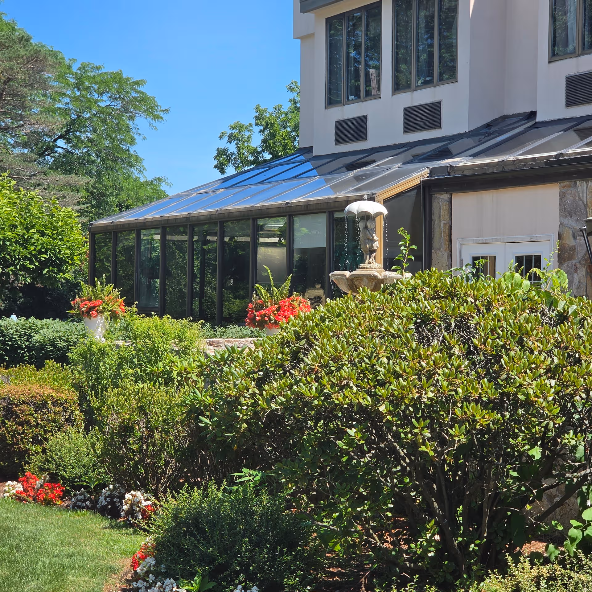 Exterior view of a cream building with a glass sunroom and manicured garden