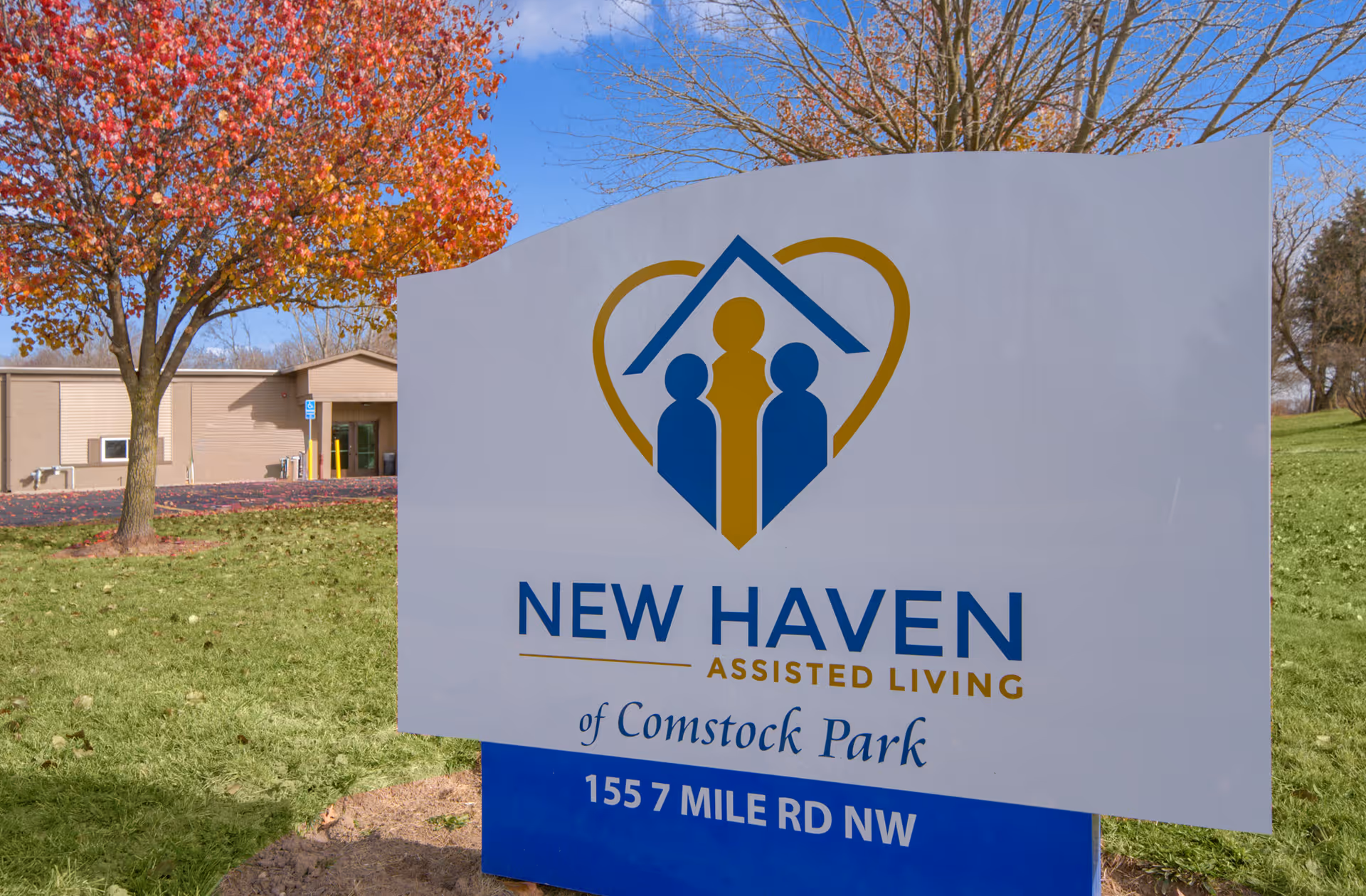 New Haven Assisted Living sign on a grassy lawn with autumn trees and building in background.
