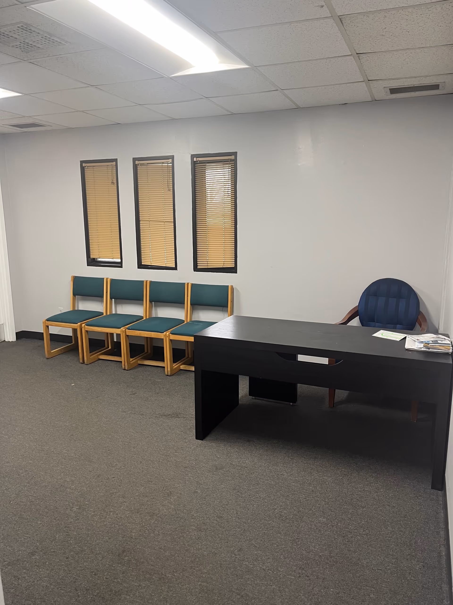 Interior office/waiting area with teal chairs, a dark desk, and three window panels.
