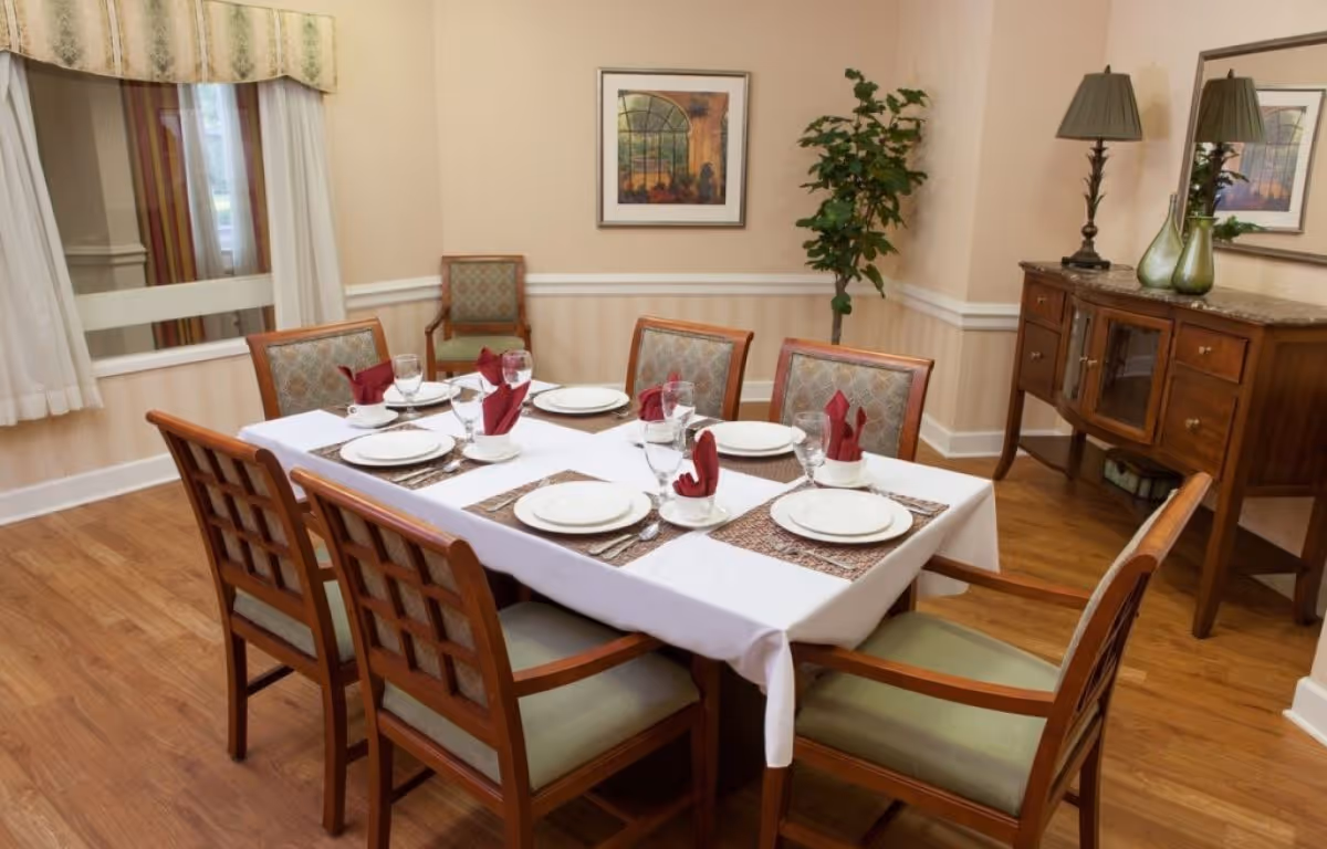 A formal dining room with a table set for six, wooden chairs, a sideboard, lamp, and wall art.