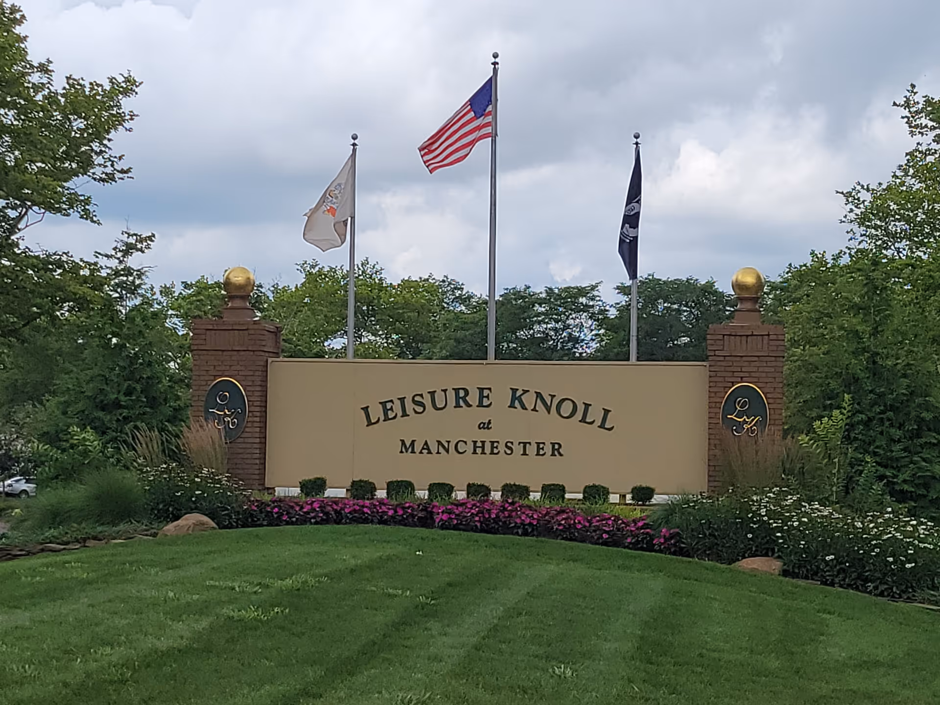 Entrance sign for Leisure Knoll at Manchester with flags and landscaped lawn.