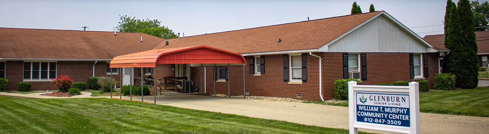 A brick senior living facility exterior with a red canopy entrance and a sign.